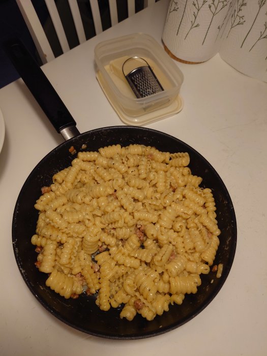 Stekt pasta i panna, riven ost i burk, köksinteriör, matlagning.