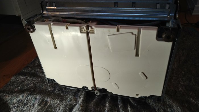 Vit diskmaskin liggande öppen på golvet, synlig baksida och inre mekanik.