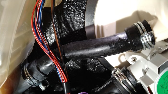 Maskinens inre med slangar, kablar och komponenter, möjligen en del av vitvaror eller utrustning.