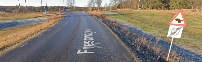 Lantlig väg, trafikskyltar för vägarbete och korsande djur, "Frösåvägen" målat på asfalten, frostdraperat gräs.