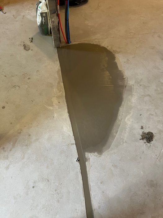 Vattenläcka på betonggolv; verktyg och kablar syns; potentiellt under konstruktion eller reparation.