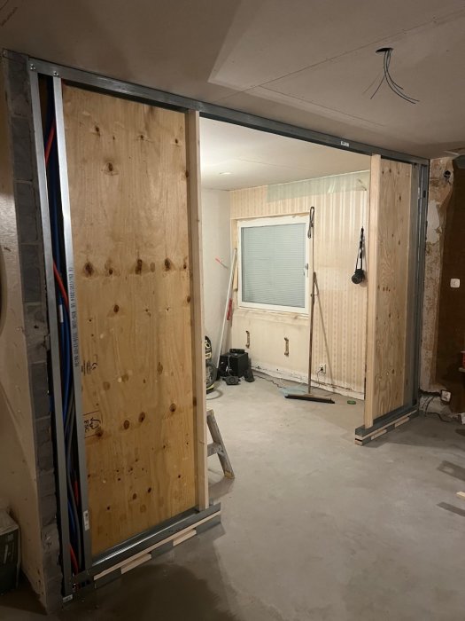 En pågående renovering visar en öppen träskjutdörr, obehandlade väggar och verktyg i ett ofärdigt rum.
