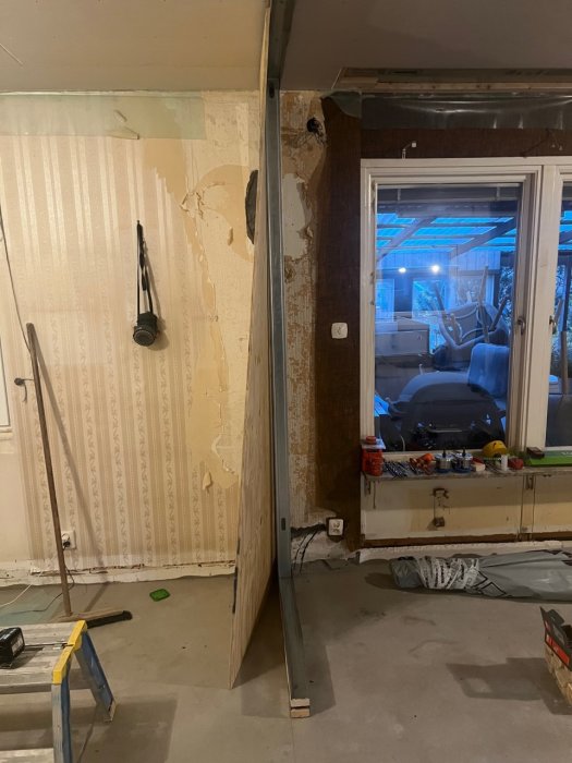 Renoveringsarbete, nakna väggar, byggmaterial, verktyg, inomhus, skymning synlig genom fönster, oavslutat projekt.