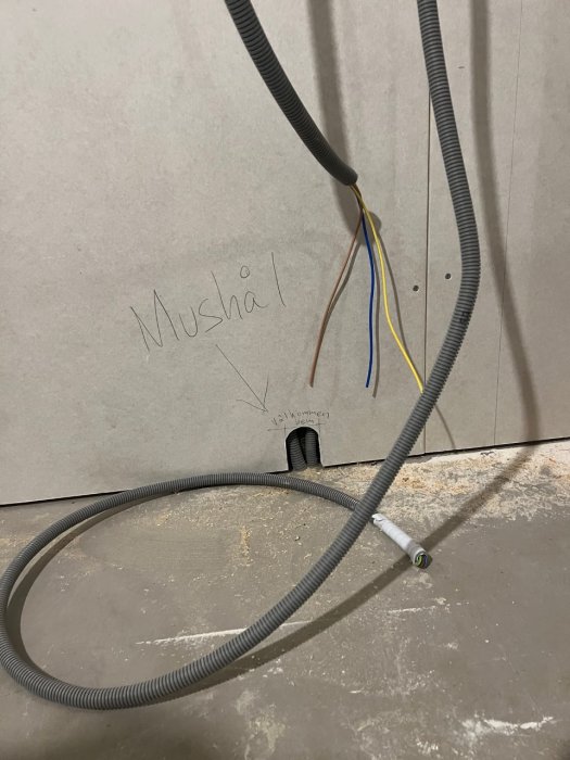 Elektriska kablar i flexibla skyddsrör, ordet "Musshål" skrivet, vägggenomföring, grå bakgrund, obehandlat område.
