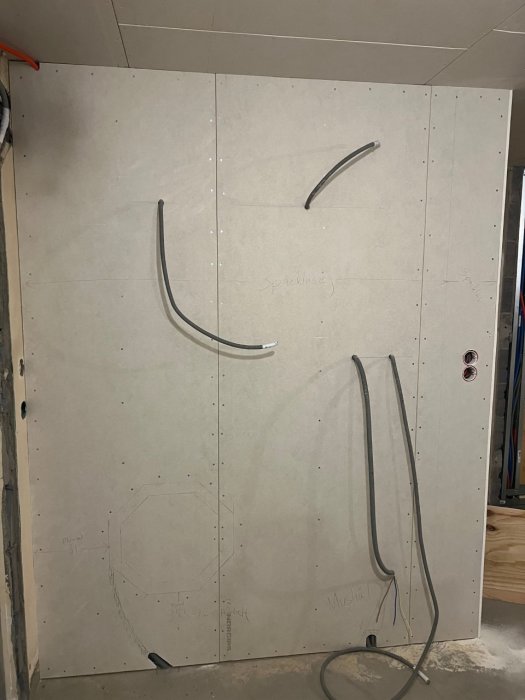 Byggarbetsplats med gipsvägg och elektriska kablar som sticker ut, anteckningar och märkningar för installationer syns.
