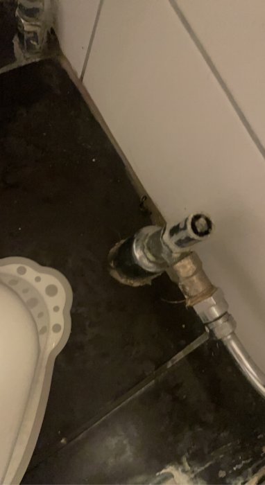 En radiator med anslutande rör mot en smutsig golv och vägg, del av plastmatta syns.