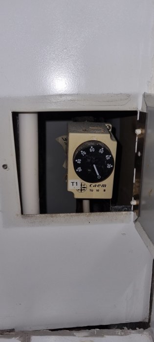 En gammal termostat i en nisch med sliten vit färg och smuts.