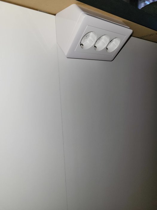 Vit taklampa med tre spotlights i ett hörn mot en vit vägg.