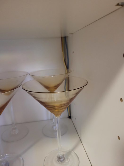 Tre martiniglas med brun vätska står på en vit hylla inne i ett skåp.