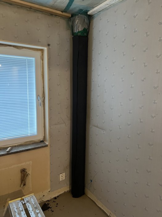 Renoveringsarbete, rörklädd i svart, oavslutat golv och väggar, sprucket fönster, kala elektriska uttag, byggmaterial rester.