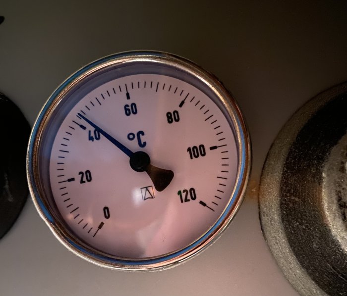 Analog termometer visande ungefär 20 grader Celsius, inklämd mellan objekt i mörk miljö.