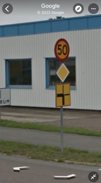 Industribyggnad med trafikskyltar för hastighetsbegränsning och vägkorsning, suddig, sannolikt från Google Street View.