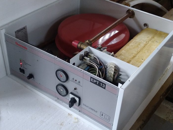 Öppnad värmepump med kontrollpanel, mätare och röd ackumulatortank, visar interna komponenter och isolering.