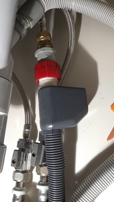 VVS-installation under diskbänk, med avstängningsventiler, flexslangar och rörkopplingar. Skuggor och ljus på ytan.