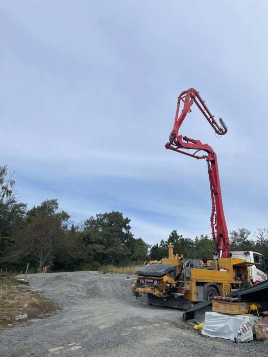 En betongpump på en lastbil på en grusväg med träd och molnig himmel.