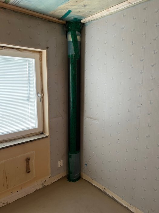 Grön byggnadsstöttning i hörn av rum med tapeter och oavslutad renovering.