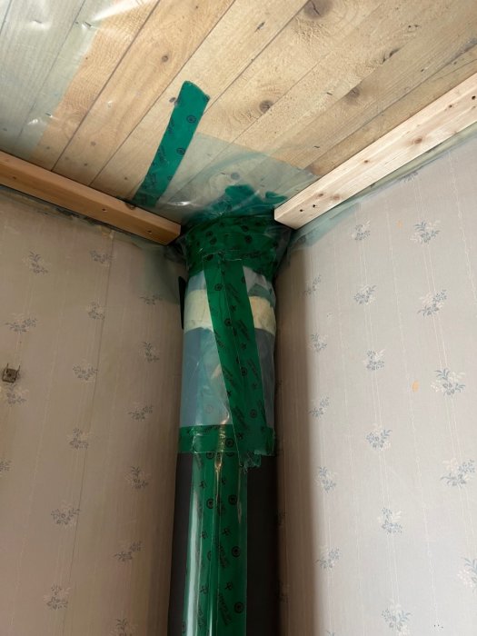 Installationsrör i hörn med trä och brandskydd, tapetvägg, byggplast, oavslutade byggarbeten eller renovering.