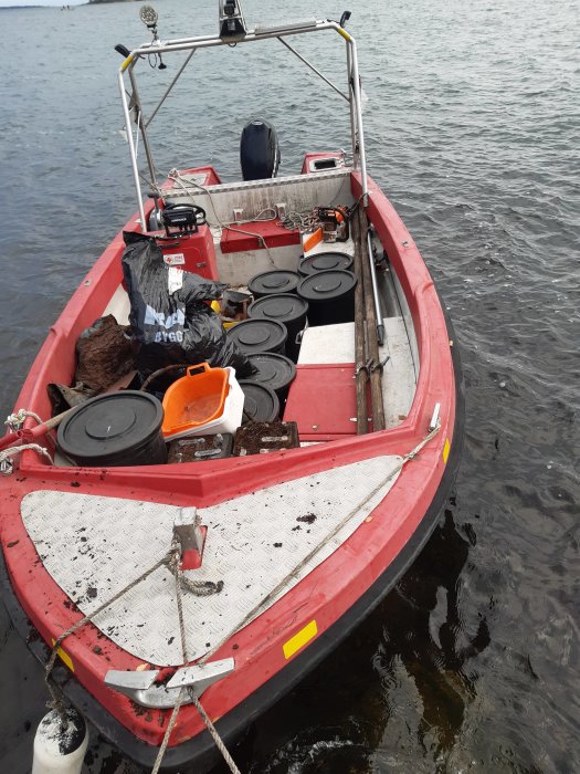 Röd arbetsbåt fylld med verktyg och utrustning flyter på vatten.