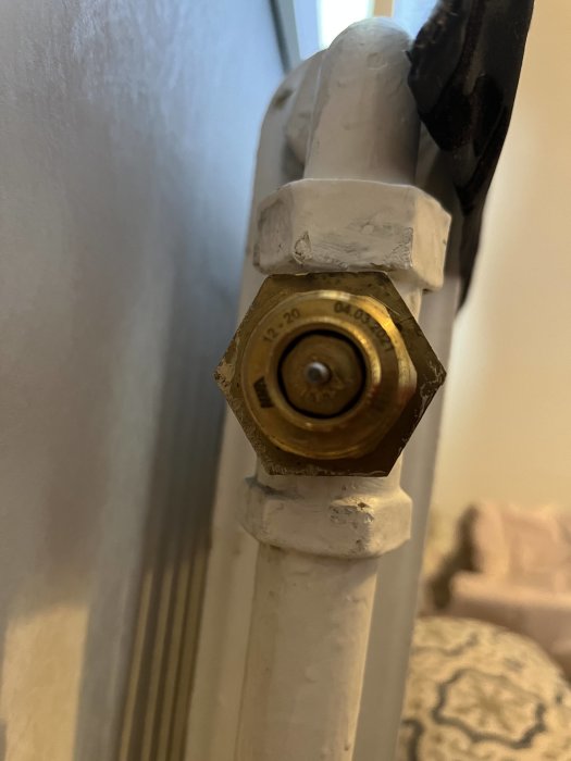 Radiatortermostat i förgrunden, målad vit radiatorbakgrund, närbild, fokus på termostatens inställningar.