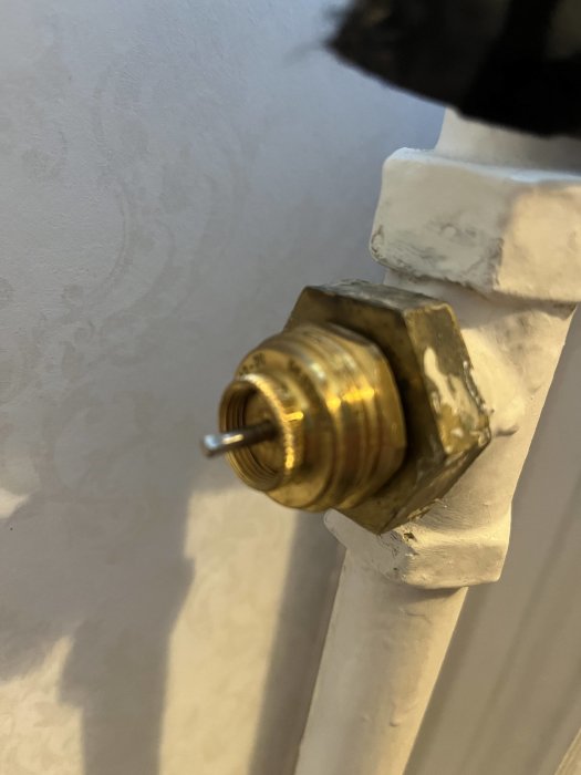 Mässingsventil närbild, vitmålad röranslutning, vägg bakgrund, inomhus, ingen knopp, delvis oskarp, renoveringsdetalj.