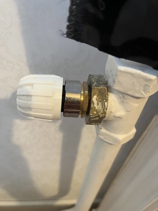 Termostatventil på radiator, vita och metallkomponenter, vägg, anslutning till värmesystem.