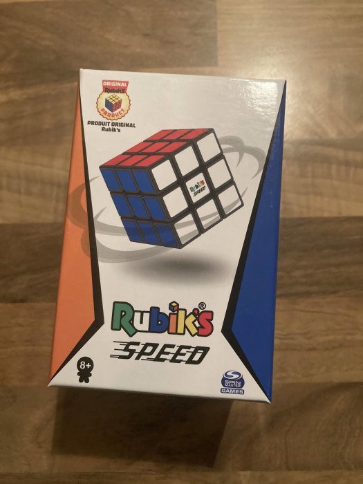 En Rubik's Speed kubförpackning på ett golv. Logotyp, åldersrekommendation "8+", och Spin Master-spelnotering syns.