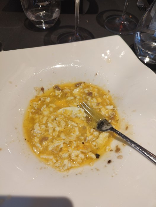 En tallrik med rester av risrätt och sås, en gaffel, i bakgrunden glas och vinglas.