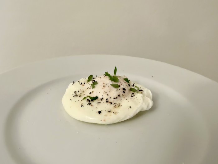Pocherat ägg på vit tallrik, toppat med svartpeppar och gröna kryddor.