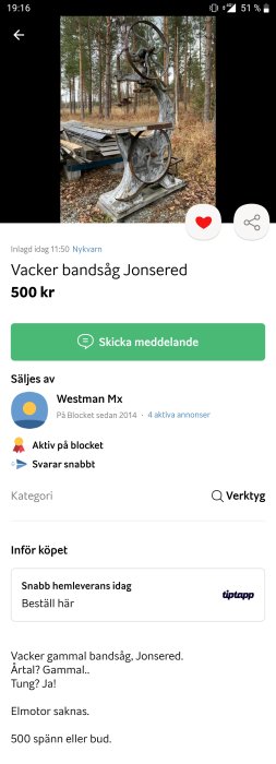 Gammal bandsåg, utomhus, saknar elmotor, till salu för 500 kronor eller högstbjudande, skogsomgivning i bakgrunden.