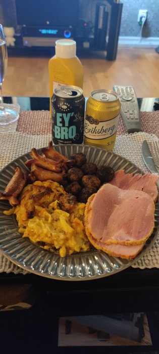 Tallrik med bacon, köttbullar, stekt potatismos, skinka; ölburkar; juiceflaska; fjärrkontroll; hemmiljö.