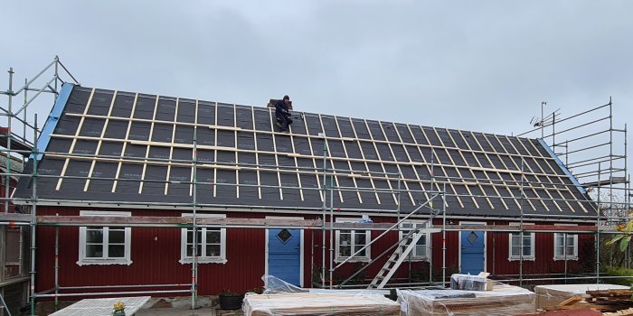 Installation av solpaneler på taket till ett rött hus, med byggnadsställning och en arbetare.