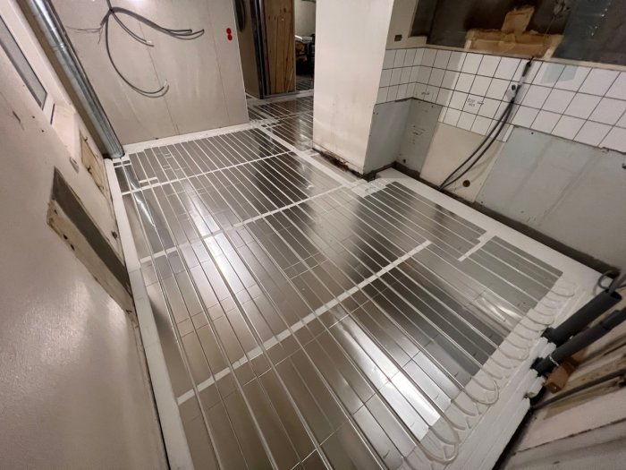En trappa i en industriell miljö med vita kakelväggar och rörledningar.
