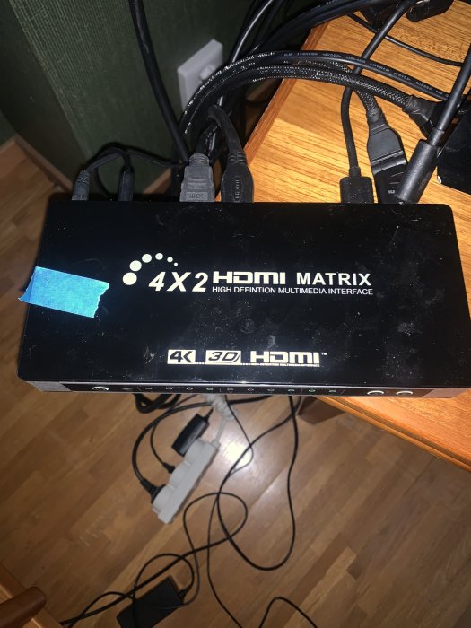 En enhet märkt "4x2 HDMI Matrix" med flera inkopplade HDMI-kablar och tejpbit på toppen.