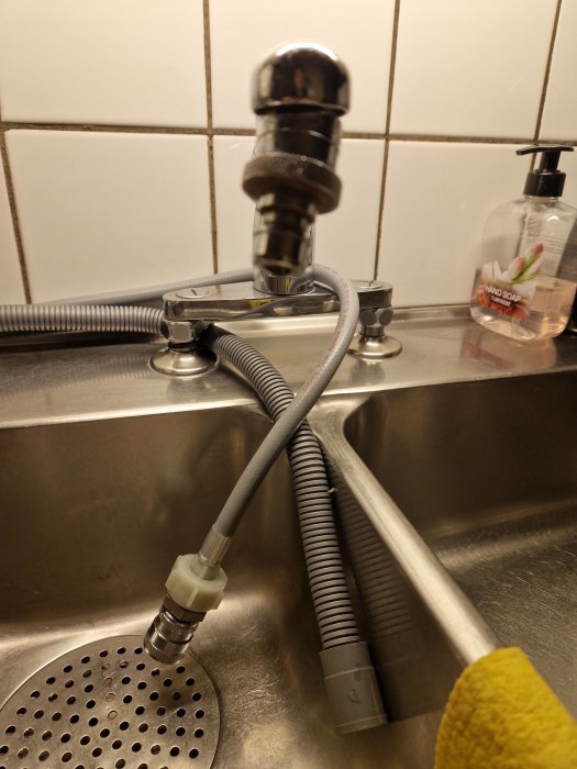 Köksvask med flexibel kran, slangar, handtvål, och en gul disktrasa.