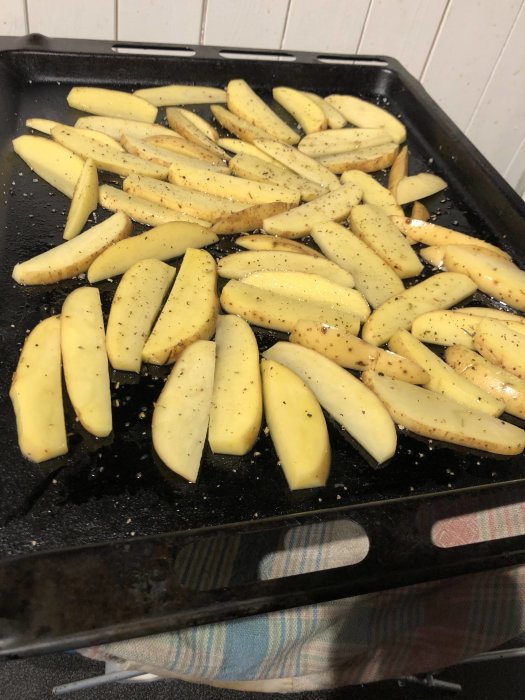 Ugnsklara potatisklyftor kryddade med peppar på en bakplåt, redo att tillagas.