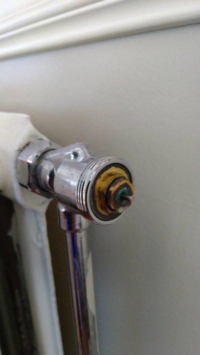 En närbild av en äldre, korroderad termostatventil på en radiator, behöver underhåll eller utbyte.