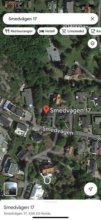 Satellitbild över bostadsområde med markerad adress, kartikoner, skog och vägar.