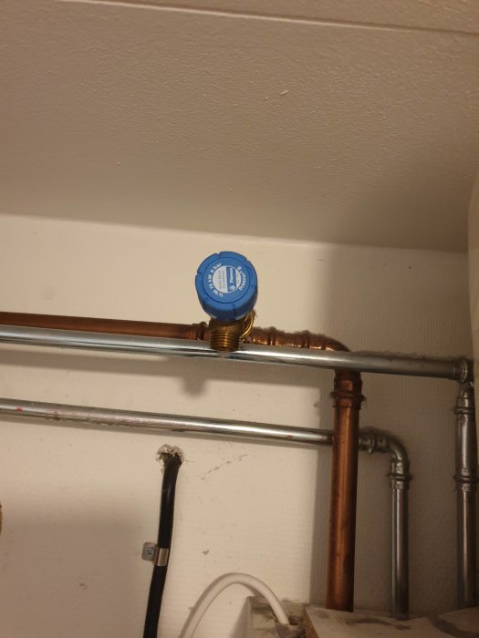 Vattenrör med blå ventilhatt, kopplingar och fästen på vit vägg.