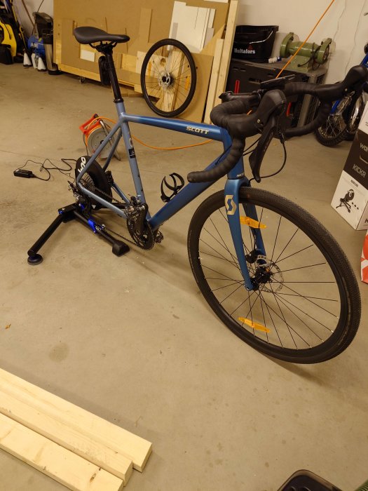 Blå landsvägscykel på ställning i garage, omgivet av verktyg och cykeldelar.