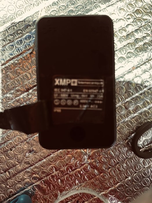 En svart elektronisk enhet på bubbelplast. Märket är synligt. Bilden är suddig och mörk.