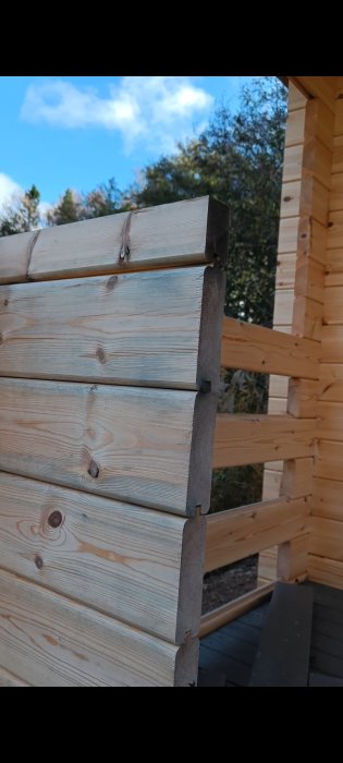 Träkonstruktion, stockar, knutar, metalldekor, ommålad, träbyggnad, klar himmel, gröna träd, traditionellt snickeri.