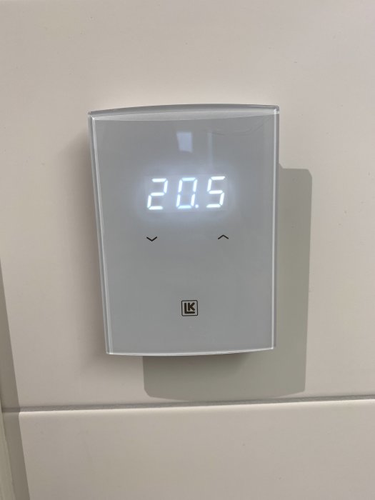 Digital termostat visar 20.5 grader Celsius på en vägg. Enkel, modern design.
