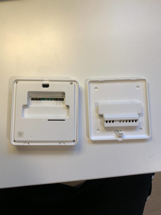 Två vita plastenheter, troligen termostater eller regulatorer, öppnade och monterade på en vägg.