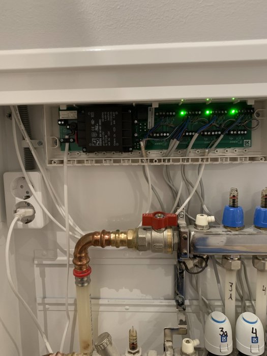 Värmesystemskåp med kopplingar, elektroniska kretsar, ventiler och indikerande gröna lysdioder.