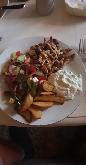 Tallrik med grillad kyckling, klyftpotatis, tzatziki, grönsallad. Måltid serverad, måltiden är redo att avnjutas.