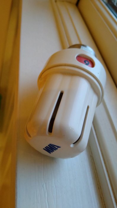 Energisnål lampa, spiralform, vit, ligger på fönsterbräda, delvis suddig bild, inomhus, dagsljus.