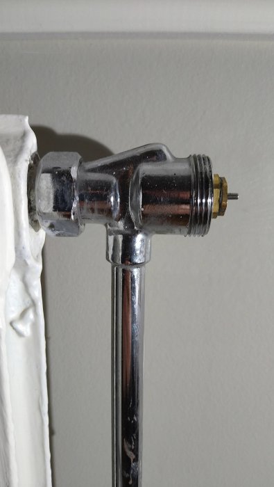 Kromad termostatventil på radiator, förinställt vinkel, vägg, rörmontage, använd, värmesystemkomponent.