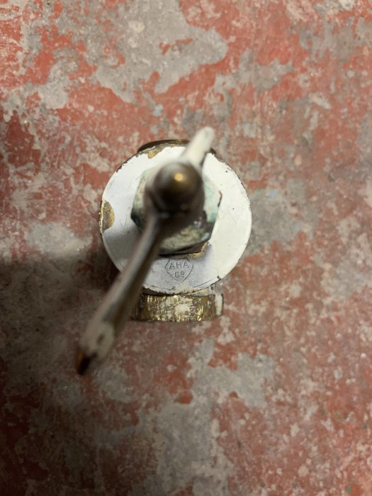 Gamla rostig vattenkran över rödaktig, fläckig betongyta. Fokus på kranens handtag.