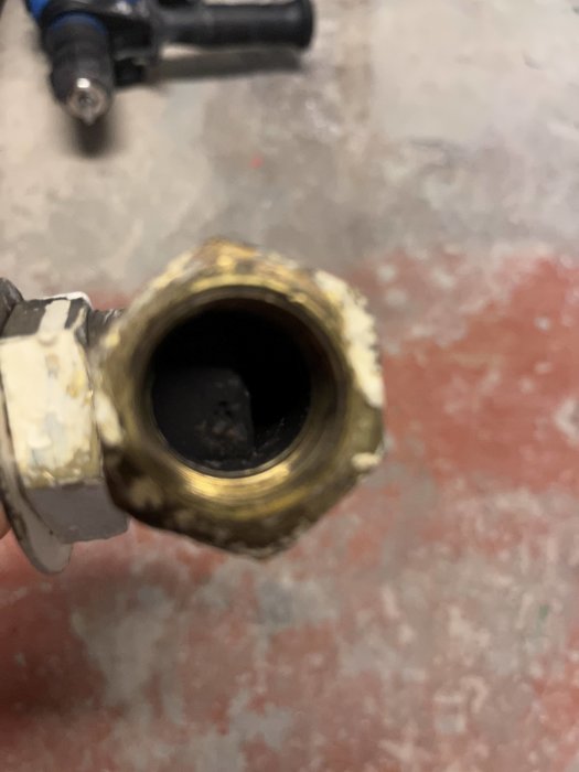 Närbild på en nedsliten metallfittings med spår av korrosion eller smuts, otydlig bakgrund.
