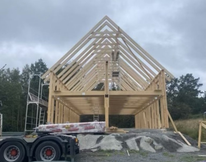 Trästomme av hus under konstruktion, byggnadsmaterial i förgrunden, molnig himmel, obefintliga väggar och tak.